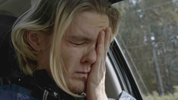 Young man with anxiety driving car. Stock. Close-up of man conveys emotions while driving car. Man with panic attack driving car on side of road.