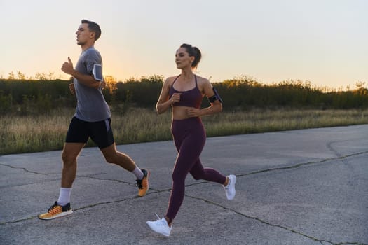 A handsome young couple running together during the early morning hours, with the mesmerizing sunrise casting a warm glow, symbolizing their shared love and vitality.