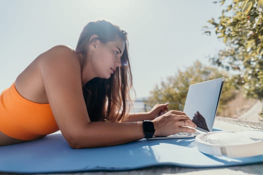 Digital nomad, Business woman working on laptop by the sea. Pretty lady typing on computer by the sea at sunset, makes a business transaction online from a distance. Freelance, remote work on vacation