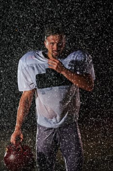 American Football Field: Lonely Athlete Warrior Standing on a Field Holds his Helmet and Ready to Play. Player Preparing to Run, Attack and Score Touchdown. Rainy Night with Dramatic Fog, Blue Light.