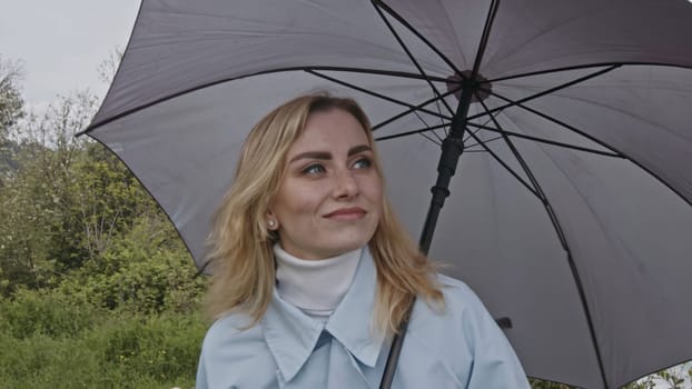 Portrait of cute romantic blonde woman smiling in green spring park. Stock clip. Young woman with grey umbrella