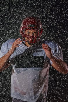 American Football Field: Lonely Athlete Warrior Standing on a Field Holds his Helmet and Ready to Play. Player Preparing to Run, Attack and Score Touchdown. Rainy Night with Dramatic Fog, Blue Light.