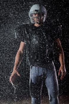 American Football Field: Lonely Athlete Warrior Standing on a Field Holds his Helmet and Ready to Play. Player Preparing to Run, Attack and Score Touchdown. Rainy Night with Dramatic Fog, Blue Light.