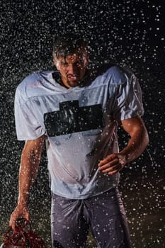 American Football Field: Lonely Athlete Warrior Standing on a Field Holds his Helmet and Ready to Play. Player Preparing to Run, Attack and Score Touchdown. Rainy Night with Dramatic Fog, Blue Light.