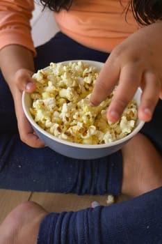 child hand pick popcorn sitting on floor .