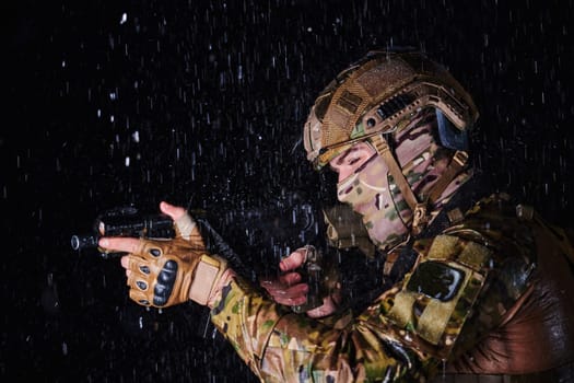 Army soldier in Combat Uniforms with an assault rifle, plate carrier and combat helmet going on a dangerous mission on a rainy night