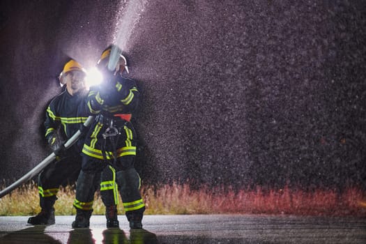 Firefighters using a water hose to eliminate a fire hazard. Team of female and male firemen in dangerous rescue mission