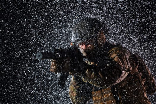 Army soldier in Combat Uniforms with an assault rifle, plate carrier and combat helmet going on a dangerous mission on a rainy night