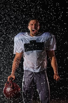 American Football Field: Lonely Athlete Warrior Standing on a Field Holds his Helmet and Ready to Play. Player Preparing to Run, Attack and Score Touchdown. Rainy Night with Dramatic Fog, Blue Light.