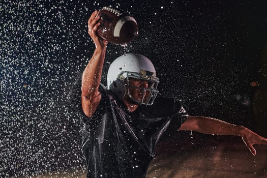 American Football Field: Lonely Athlete Warrior Standing on a Field Holds his Helmet and Ready to Play. Player Preparing to Run, Attack and Score Touchdown. Rainy Night with Dramatic Fog, Blue Light.