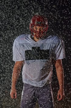 American Football Field: Lonely Athlete Warrior Standing on a Field Holds his Helmet and Ready to Play. Player Preparing to Run, Attack and Score Touchdown. Rainy Night with Dramatic Fog, Blue Light.