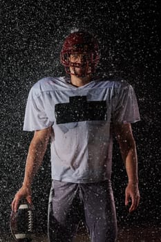 American Football Field: Lonely Athlete Warrior Standing on a Field Holds his Helmet and Ready to Play. Player Preparing to Run, Attack and Score Touchdown. Rainy Night with Dramatic Fog, Blue Light.