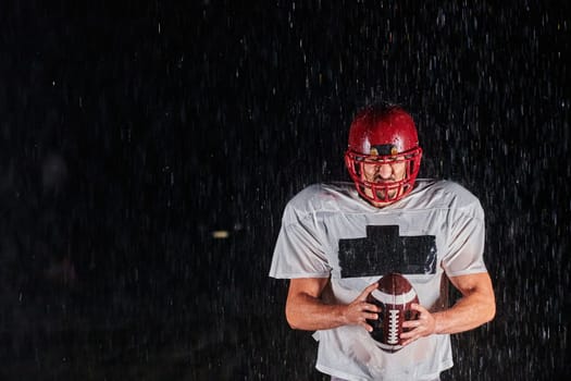 American Football Field: Lonely Athlete Warrior Standing on a Field Holds his Helmet and Ready to Play. Player Preparing to Run, Attack and Score Touchdown. Rainy Night with Dramatic Fog, Blue Light.