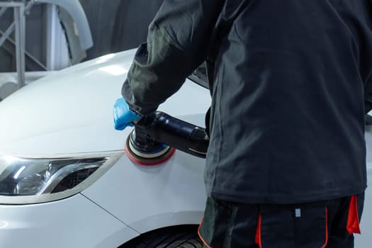 Serviceman polishing car body with machine in a workshop