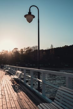 White Old wood bridge pier against beautiful sunset sky natural background, backdrop wallpaper multipurpose sea scene. White benches no people in Gdynia Orlowo, Poland. Wooden pier, molo with marina and beach Touristic destination