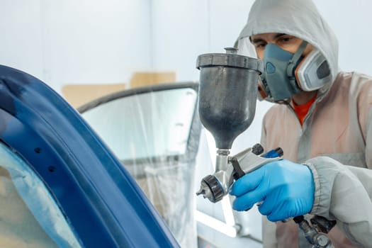 automobile repairman painter hand in protective glove with airbrush pulverizer painting car body in paint chamber