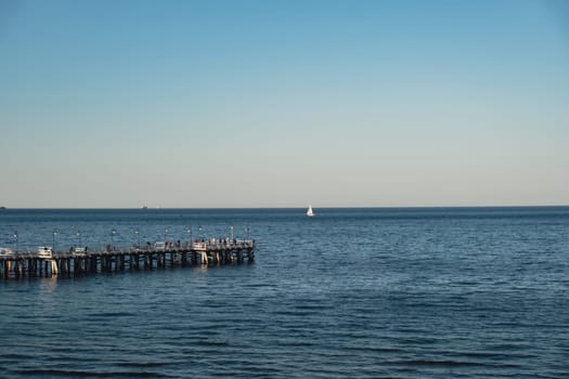 Storm sea waves empty wooden pier in dramatic blue sky background. Seascape with running splashing sea waves. Sandy beach vacation getaway in Gdansk Poland. Copy space for your text