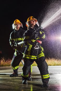 Firefighters using a water hose to eliminate a fire hazard. Team of female and male firemen in dangerous rescue mission