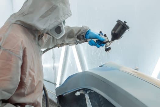 automobile repairman painter hand in protective glove with airbrush pulverizer painting car body in paint chamber