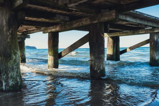 Storm sea waves under wooden pier in dramatic background wallpaper design. Seascape with running splashing sea waves. Sandy beach vacation getaway in Gdansk Poland. Copy space for your text