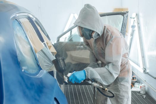 automobile repairman painter hand in protective glove with airbrush pulverizer painting car body in paint chamber