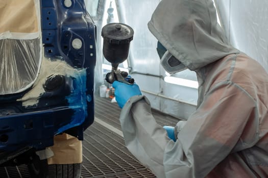 automobile repairman painter hand in protective glove with airbrush pulverizer painting car body in paint chamber