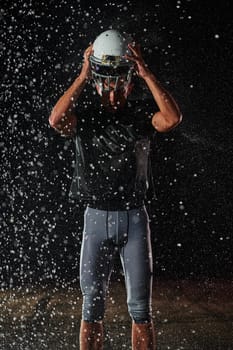 American Football Field: Lonely Athlete Warrior Standing on a Field Holds his Helmet and Ready to Play. Player Preparing to Run, Attack and Score Touchdown. Rainy Night with Dramatic Fog, Blue Light.