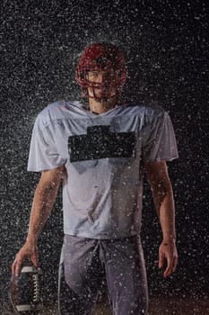 American Football Field: Lonely Athlete Warrior Standing on a Field Holds his Helmet and Ready to Play. Player Preparing to Run, Attack and Score Touchdown. Rainy Night with Dramatic Fog, Blue Light.