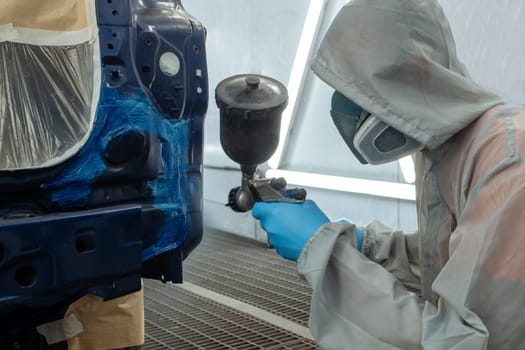 automobile repairman painter hand in protective glove with airbrush pulverizer painting car body in paint chamber