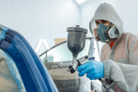 automobile repairman painter hand in protective glove with airbrush pulverizer painting car body in paint chamber