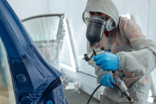 automobile repairman painter hand in protective glove with airbrush pulverizer painting car body in paint chamber