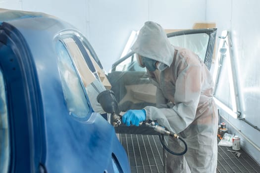 Professional car painter is painting in garage by airbrush