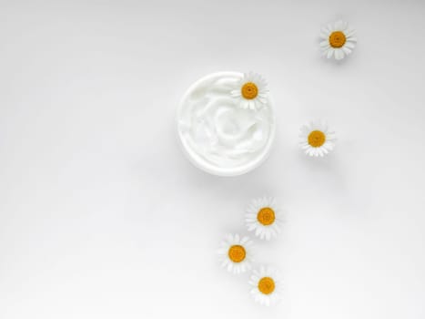 Open jar of white hand or body cream with chamomile flowers on white background. Top view composition with copy space. For skincare and beauty product concept. High quality photo