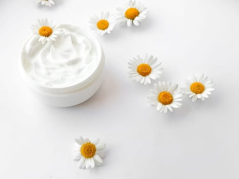 Open jar of white hand or body cream with chamomile flowers on white background. Flat lay composition. For skincare and beauty product concept. High quality photo