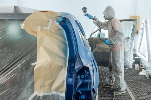 automobile repairman painter hand in protective glove with airbrush pulverizer painting car body in paint chamber