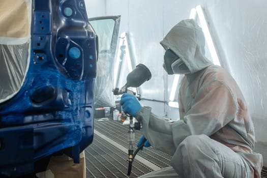 automobile repairman painter hand in protective glove with airbrush pulverizer painting car body in paint chamber