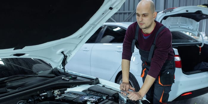 A male automech is inspecting the car's engine. Car service and car repair.