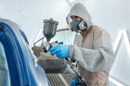 automobile repairman painter hand in protective glove with airbrush pulverizer painting car body in paint chamber