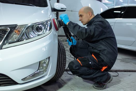 Serviceman polishing car body with machine in a workshop