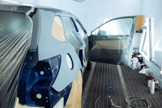 automobile repairman painter hand in protective glove with airbrush pulverizer painting car body in paint chamber