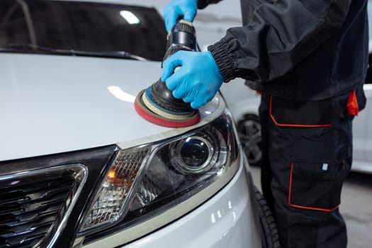 Serviceman polishing car body with machine in a workshop