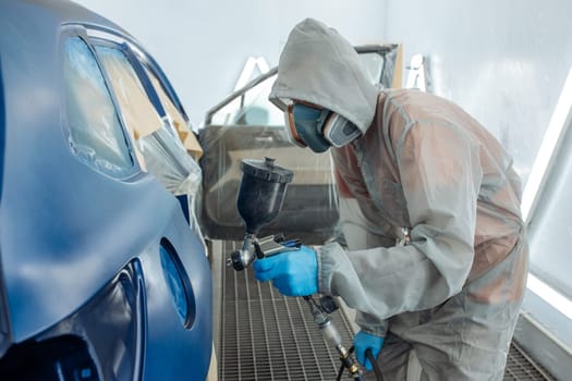 automobile repairman painter hand in protective glove with airbrush pulverizer painting car body in paint chamber