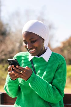 young african woman smiling happy using mobile phone outdoors, concept of technology of communication and modern lifestyle