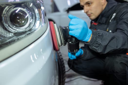 Serviceman polishing car body with machine in a workshop