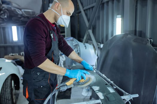 Sanding a car body part with electrical grinder machine before painting, vehicle body repair service