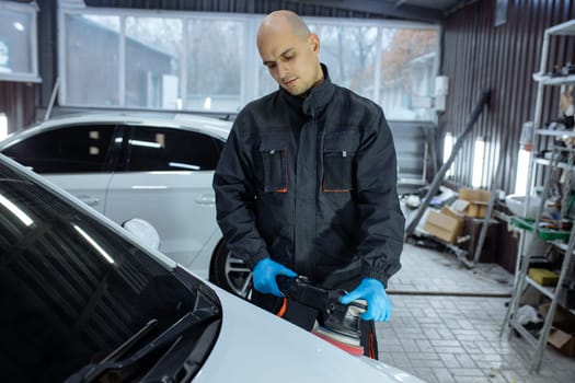 Serviceman polishing car body with machine in a workshop