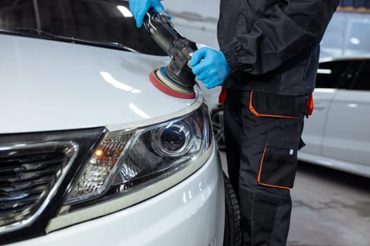 Serviceman polishing car body with machine in a workshop