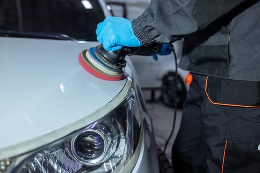 Serviceman polishing car body with machine in a workshop