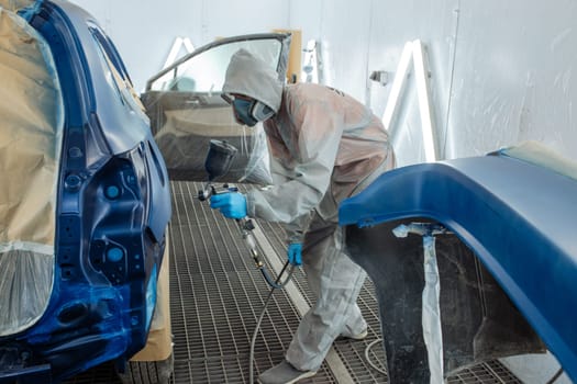 automobile repairman painter hand in protective glove with airbrush pulverizer painting car body in paint chamber