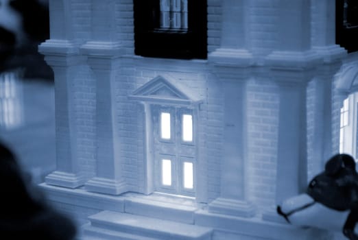 Model of building with white and black color, windows with light shining, created by 3D printer from molten plastic. Prototype printed on 3D printer brick building with columns and glowing windows.